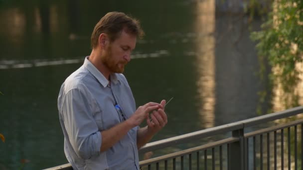 Pria Dewasa Memakai Kacamata Menggunakan Smartphone Dekat Sungai — Stok Video