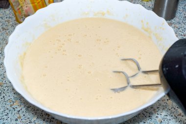 Mutfakta beyaz bir kasede karıştırıcıyla sıvı hamur dövmek..