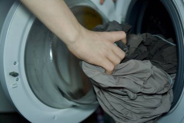 Çamaşırları modern bir çamaşır makinesine koyan insanların yakın çekimi. Ev işleri, çamaşır günü, ev işi ve ev aletleri kullanımı kavramı. Koyu Giysiler Yükleniyor