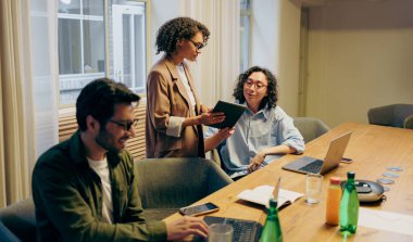 Tableti Tablo 'da inceleyen meslektaşlar, proje güncellemelerini ve sonraki adımları dizüstü bilgisayarlar açık ve notlarla tartışır