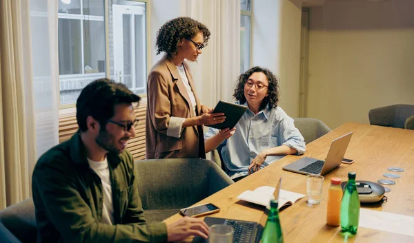 Tableti Tablo 'da inceleyen meslektaşlar, proje güncellemelerini ve sonraki adımları dizüstü bilgisayarlar açık ve notlarla tartışır