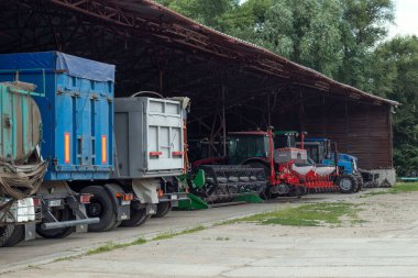 Tarım makineleri ve kamyonlar bir çiftlikteki hangarın altında park halinde. tarımsal operasyonlar, lojistik ve depolama pahalı ağır ekipmanların sezon dışında veya hazırlık aşamasında