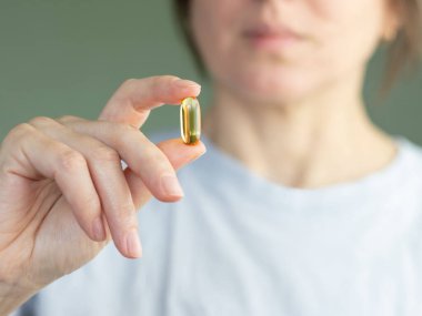 Kadının elinin Omega-3 ile şeffaf kapsülü tutarken yakın çekimi. Kadın, sağlığını korumak için vitaminli kapsül veya beslenme takviyesi alıyor.