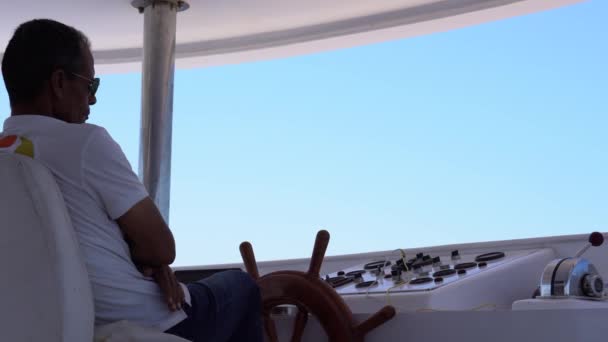 En kapten i vit T-shirt styr båten vid rodret.. — Stockvideo