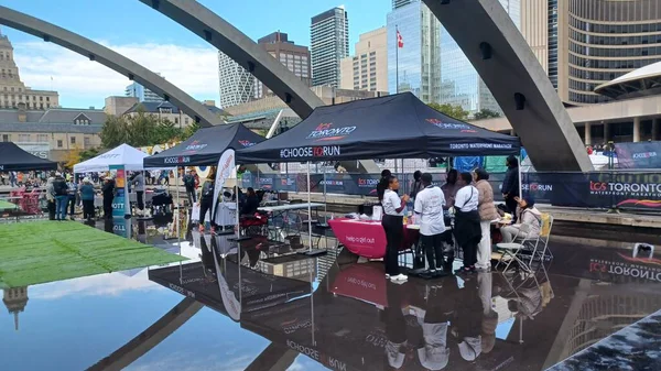 Toronto, ON, Kanada - 18 Ekim 2025: Bir belediye binasının sembolik kemerleri, satıcı çadırlarıyla düzenlenen bir maraton etkinliği sırasında bir havuza yansıyor