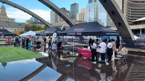 Toronto, ON, Kanada - 18 Ekim 2025: Bir belediye binasının sembolik kemerleri, satıcı çadırlarıyla düzenlenen bir maraton etkinliği sırasında bir havuza yansıyor