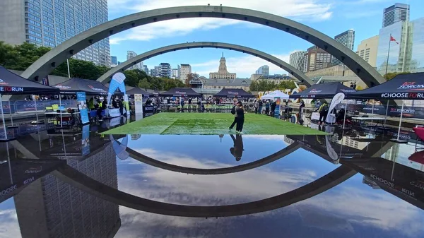 Toronto, ON, Kanada - 18 Ekim 2025: Bir belediye binasının sembolik kemerleri, satıcı çadırlarıyla düzenlenen bir maraton etkinliği sırasında bir havuza yansıyor