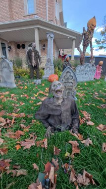 Toronto, ON, Kanada - 22 Ekim 2025 Yerden korkunç bir zombi süslemesi yükseliyor mezar taşları ve sonbahar yapraklarıyla dolu bir bahçede.