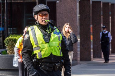Toronto, ON, Kanada - 24 Ekim 2025: Emniyet yeleği giymiş bir polis memuru şehir sokaklarında görev yaparken düdük çalıyor.
