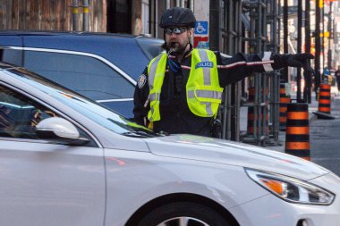 Toronto, ON, Kanada - 24 Ekim 2025: Emniyet yeleği giymiş bir polis memuru işlek bir şehir caddesinde araba trafiğini yönetti.