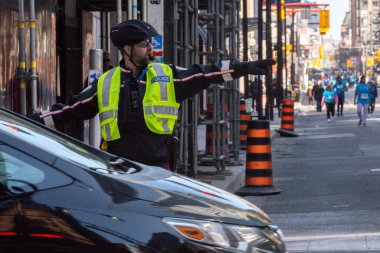 Toronto, ON, Kanada - 24 Ekim 2025: Emniyet yeleği giymiş bir polis memuru işlek bir şehir caddesinde araba trafiğini yönetti.