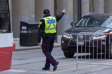 Toronto, ON, Kanada - 24 Ekim 2025: Emniyet yeleği giymiş bir polis memuru işlek bir şehir caddesinde araba trafiğini yönetti.