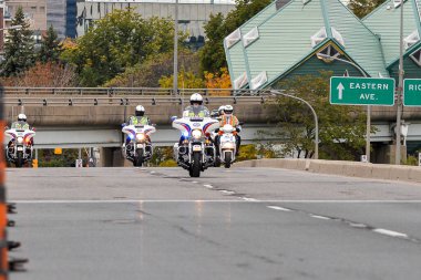 Toronto, ON, Kanada - 24 Ekim 2025: Kasklı ve güvenlik yeleği giymiş bir polis memuru şehir yolunda beyaz bir motosiklet sürüyor.