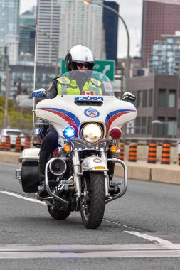 Toronto, ON, Kanada - 24 Ekim 2025: Kasklı ve güvenlik yeleği giymiş bir polis memuru şehir yolunda beyaz bir motosiklet sürüyor.