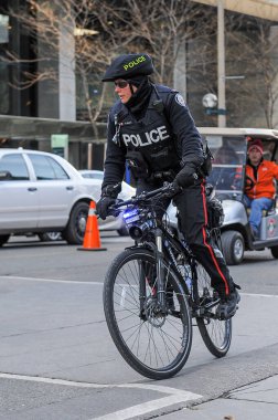 Toronto, ON, Kanada - 24 Ekim 2025: Üniformalı bir polis memuru bisiklet üzerinde bir şehir caddesinde devriye geziyor.