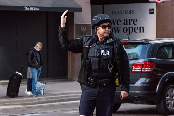 Toronto, ON, Kanada - 24 Ekim 2025: Emniyet yeleği giymiş bir polis memuru işlek bir şehir caddesinde araba trafiğini yönetti.
