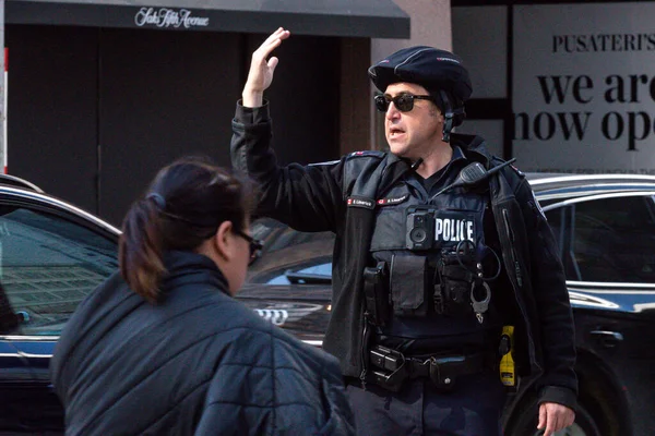 Toronto, ON, Kanada - 24 Ekim 2025: Emniyet yeleği giymiş bir polis memuru işlek bir şehir caddesinde araba trafiğini yönetti.