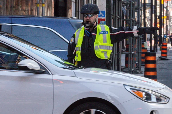 Toronto, ON, Kanada - 24 Ekim 2025: Emniyet yeleği giymiş bir polis memuru işlek bir şehir caddesinde araba trafiğini yönetti.
