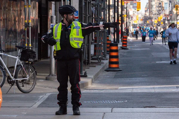 Toronto, ON, Kanada - 24 Ekim 2025: Emniyet yeleği giymiş bir polis memuru işlek bir şehir caddesinde araba trafiğini yönetti.