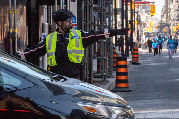 Toronto, ON, Kanada - 24 Ekim 2025: Emniyet yeleği giymiş bir polis memuru işlek bir şehir caddesinde araba trafiğini yönetti.