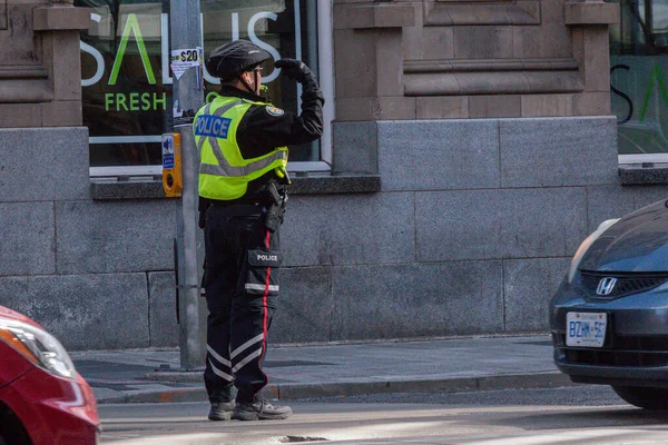 Toronto, ON, Kanada - 24 Ekim 2025: Emniyet yeleği giymiş bir polis memuru işlek bir şehir caddesinde araba trafiğini yönetti.