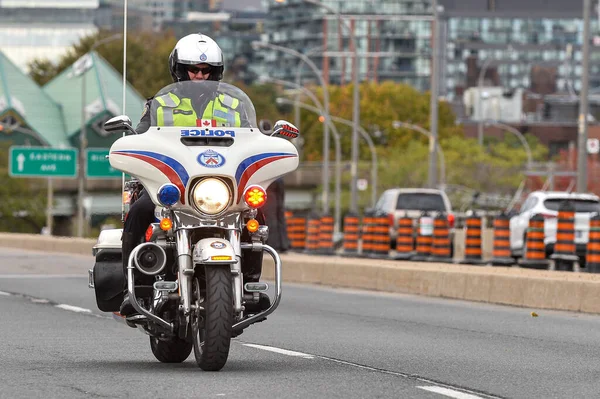 Toronto, ON, Kanada - 24 Ekim 2025: Kasklı ve güvenlik yeleği giymiş bir polis memuru şehir yolunda beyaz bir motosiklet sürüyor.