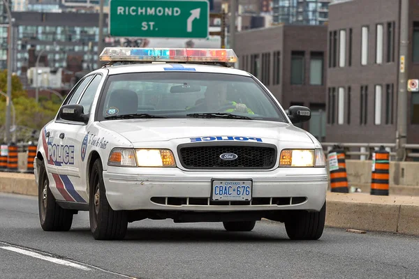 Toronto, ON, Kanada - 24 Ekim 2025: Işıkları açık beyaz bir polis kruvazörü arka planda şehir silüeti olan bir şehir otoyolunda ilerliyor.