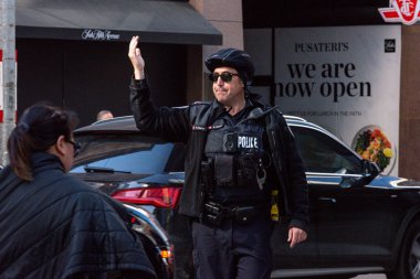 Toronto, ON, Kanada - 24 Ekim 2025: Emniyet yeleği giymiş bir polis memuru işlek bir şehir caddesinde araba trafiğini yönetti.