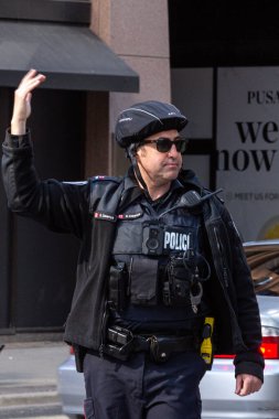 Toronto, ON, Kanada - 24 Ekim 2025: Emniyet yeleği giymiş bir polis memuru işlek bir şehir caddesinde araba trafiğini yönetti.