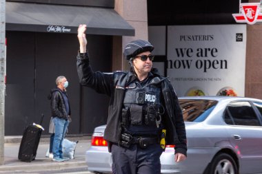 Toronto, ON, Kanada - 24 Ekim 2025: Emniyet yeleği giymiş bir polis memuru işlek bir şehir caddesinde araba trafiğini yönetti.