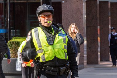 Toronto, ON, Kanada - 24 Ekim 2025: Emniyet yeleği giymiş bir polis memuru şehir sokaklarında görev yaparken düdük çalıyor.