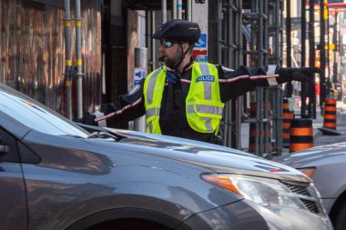 Toronto, ON, Kanada - 24 Ekim 2025: Emniyet yeleği giymiş bir polis memuru işlek bir şehir caddesinde araba trafiğini yönetti.