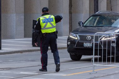Toronto, ON, Kanada - 24 Ekim 2025: Emniyet yeleği giymiş bir polis memuru işlek bir şehir caddesinde araba trafiğini yönetti.