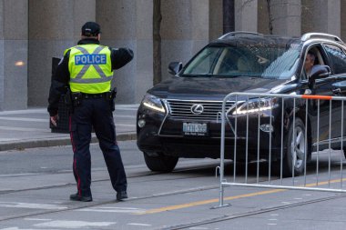 Toronto, ON, Kanada - 24 Ekim 2025: Emniyet yeleği giymiş bir polis memuru işlek bir şehir caddesinde araba trafiğini yönetti.
