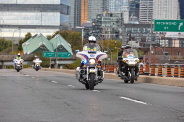 Toronto, ON, Kanada - 24 Ekim 2025: Kasklı ve güvenlik yeleği giymiş bir polis memuru şehir yolunda beyaz bir motosiklet sürüyor.