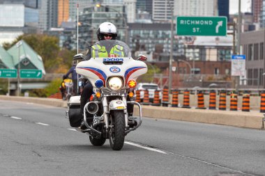 Toronto, ON, Kanada - 24 Ekim 2025: Kasklı ve güvenlik yeleği giymiş bir polis memuru şehir yolunda beyaz bir motosiklet sürüyor.