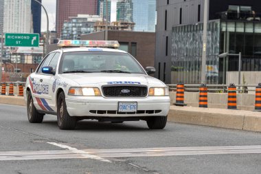 Toronto, ON, Kanada - 24 Ekim 2025: Işıkları açık beyaz bir polis kruvazörü arka planda şehir silüeti olan bir şehir otoyolunda ilerliyor.