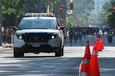 Toronto, ON, Kanada - 24 Ekim 2025: Işıkları açık beyaz bir polis cipi bir maraton sırasında şehir caddesinde koşuyor..