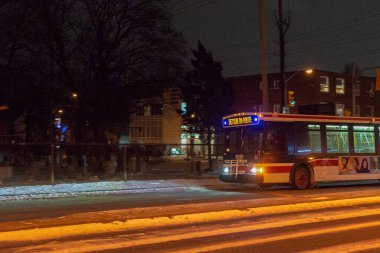 Toronto, ON, Kanada - 18 Ocak 2025: Farları açık bir toplu taşıma otobüsü gece karlı bir yolda ilerliyor.