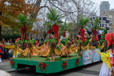 TORONONONONONTO, ONTARIO, CANADA - 23 Kasım 2025: Toronto şehir merkezindeki orijinal Noel Baba Geçidi sırasında palmiye ağaçları ve şenlik kurdeleleriyle süslenmiş renkli Karayip temalı bir şamandıra üzerinde duranlar.