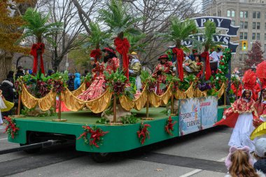 TORONONONONONTO, ONTARIO, CANADA - 23 Kasım 2025: Toronto şehir merkezindeki orijinal Noel Baba Geçidi sırasında palmiye ağaçları ve şenlik kurdeleleriyle süslenmiş renkli Karayip temalı bir şamandıra üzerinde duranlar.
