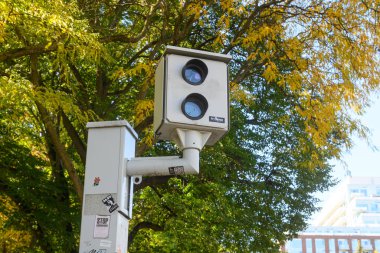 Toronto, ON, Kanada - 24 Ekim 2025: Beyaz otomatik hız kontrol kamerası (veya kırmızı ışık kamerası) yoğun yeşil ve sarı yapraklı sonbahar ağaçlarının olduğu bir kutba monte edilmiştir..