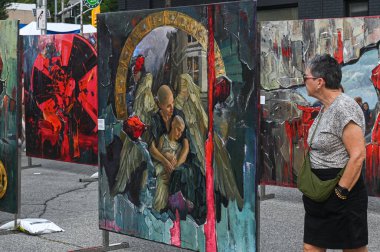 Toronto, ON, Kanada - 13 Eylül 2025: Açık hava sokak sanat sergisinde savaş, rahatlık ve yer değiştirme temalarını resmeden kadın