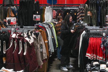 Toronto, ON, Kanada - 14 Kasım 2025: İnsanlar kapalı alanlardaki moda ve fiyatları karşılaştırarak, işlek bir perakende satış standında giysi raflarında ceket ve kıyafetlere göz atıyorlar