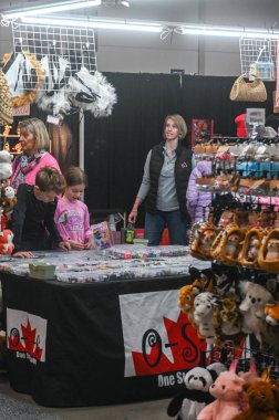 Toronto, ON, Kanada - 14 Kasım 2025: Anne ve çocuklar bir tezgahta mal tarıyorlar, oyuncak veya el işi eşyalar seçiyorlar, Kanada bayrağı logosu olan ürünler sergiliyorlar