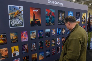 Toronto, ON, Kanada - 6 Kasım 2025: Yeşil ceketli bir adam profesyonel medya sergisinde film ve televizyon şovu posterlerine bakıyor
