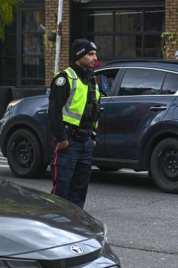 Toronto, ON, Kanada - 27 Eylül 2025: Emniyet yeleği giymiş bir polis memuru trafiğin yakınındaki bir caddede duruyor.