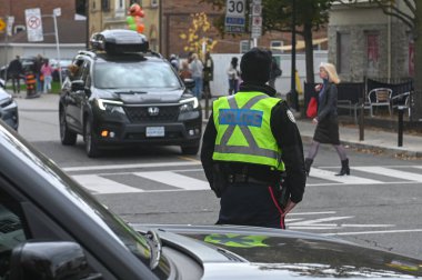 Toronto, ON, Kanada - 27 Eylül 2025: Emniyet yeleği giymiş bir polis memuru trafiğin yakınındaki bir caddede duruyor.