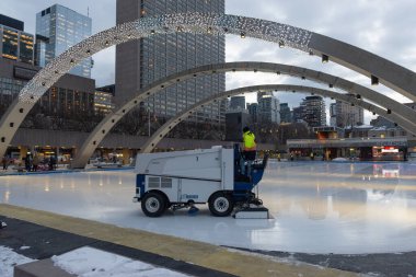 Toronto, ON, Kanada - 3 Aralık 2025: Şehir binaları ve ışıklandırılmış kemerlerle halka açık bir buz pateni pistinde buzu yeniden yüzdüren bir makine kullanan işçiler