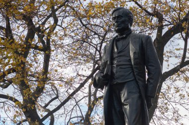 Toronto, ON, Kanada - 15 Ekim 2025 Oliver Mowat 'ın bronz heykeli, gri bir gökyüzünün altında sarı sonbahar yaprakları olan ağaçların önünde duran bir kitap tutuyor.